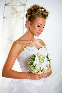 Bride with closed eyes holding bouquet while standing by arch