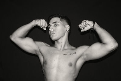 Shirtless man flexing muscles standing against black background