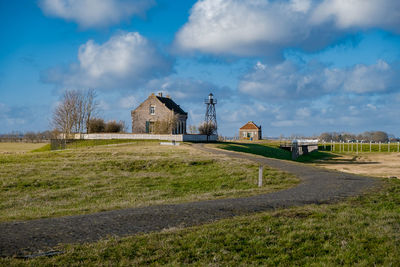 Barn on field by houses against sky