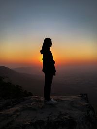 Silhouette woman standing on rock during sunset