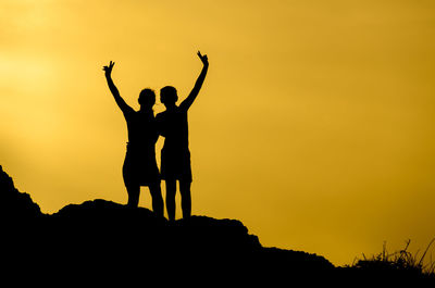 Silhouette of people on rock against sky during sunset