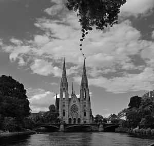 View of temple by river against cloudy sky