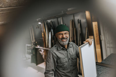 Cheerful male owner with picture frame standing at workbench