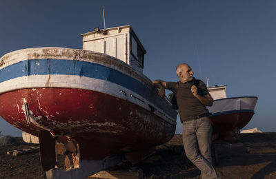 Adult man standing on beach with fishing boat during sunset. almeria, spain