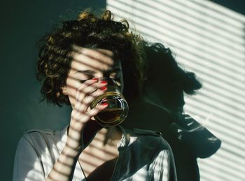 Sunlight falling on young woman drinking alcohol by wall