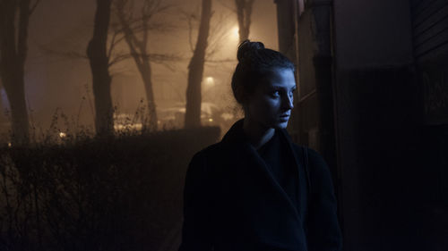 Woman standing against trees at night