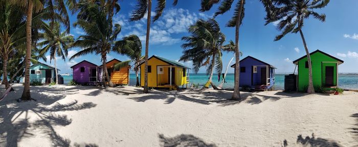 Houses on beach by palm trees against sky