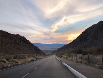 Road by mountains against sky during sunset