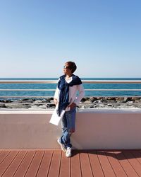 Young woman standing at beach against clear blue sky