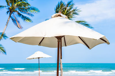Lounge chairs on beach umbrella by sea against sky