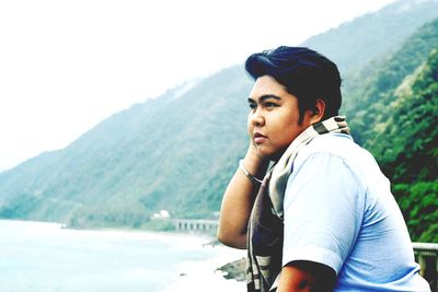 Man looking away while standing against mountain by sea