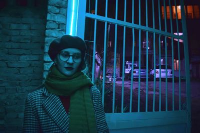 Portrait of young woman standing against illuminated wall at night