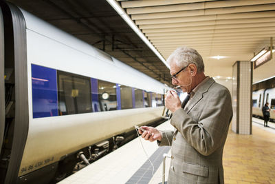 Side view of senior man talking on smart phone while standing at subway station