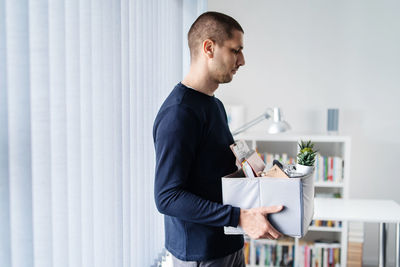 Side view of serious man carrying box in office