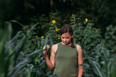 Young woman holding flower while standing against plants