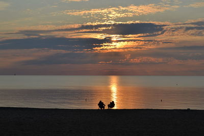 Silhouette people on beach against sky during sunset