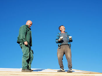 Full length of men standing against blue sky