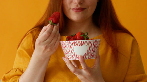 Midsection of woman holding strawberry against white background