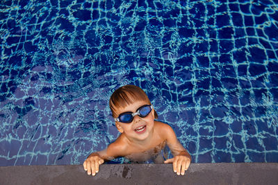 Smiling boy in goggles in water near edge of pool