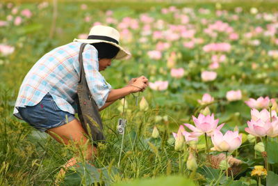 Side view of woman photographing pink lotus