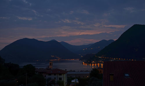 Illuminated city by sea against sky during sunset