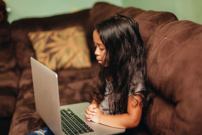 Mixed race young girl at home on the sofa using a laptop computer for learning