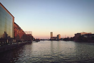 Buildings by river against sky during sunset