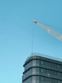 Low angle view of crane by building against clear sky