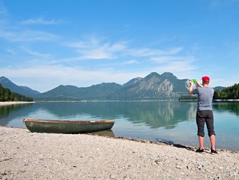 Photographer with eye at viewfinder is taking photo of lake with alps mountains in background