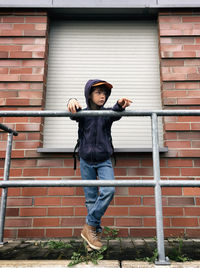 Low angle view of boy looking away while standing by railing against brick wall