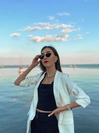 Portrait of young woman wearing sunglasses standing against sea