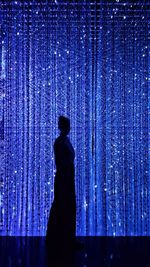 Side view of silhouette woman standing against illuminated curtain