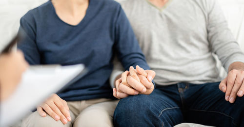 Midsection of couple holding hands while sitting on sofa