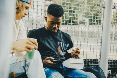 Young man using mobile phone while sitting on window