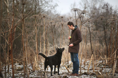 Man training dog against bare trees on land during winter