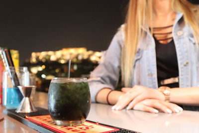 Midsection of woman with drink on table sitting in restaurant