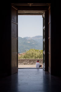 Rear view of boy sitting against sky seen through doorway