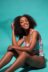 Portrait of a smiling young woman sitting against blue background