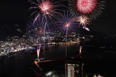 Firework display over illuminated city against sky at night