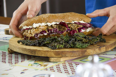 Two male hands taking pulled pork sandwich with vegetables and black cabbage chips 