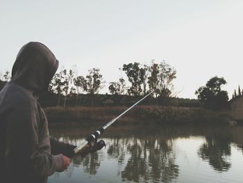 Man fishing in lake against clear sky