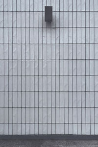 A full-frame wall made of white tiles with a loudspeaker hanging on it.