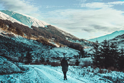 Rear view of person standing on snowcapped mountain against sky