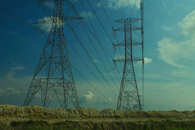 Low angle view of electricity pylon on field against sky