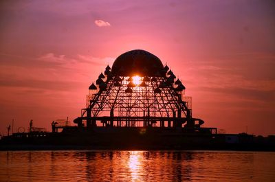 Silhouette built structure by sea against sky during sunset