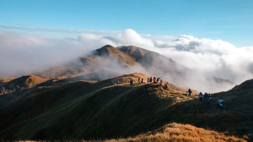 People hiking on mountain against cloudy sky