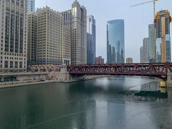 Bridge over river by buildings against sky in city
