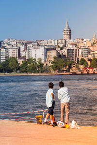 Rear view of men with umbrella on sea by city against sky