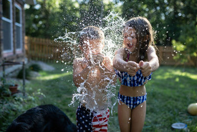 Cheerful siblings bursting water bombs while standing at backyard