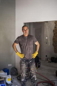 Portrait of confident male carpenter standing with arms akimbo in room at home